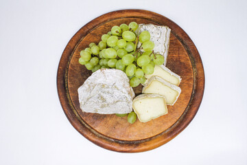 Assorted mouldy blue cheeses goat's milk on a wooden chopping board with green grapes. White background