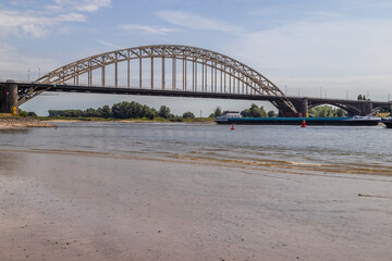 Cargo ship sails under the Waal bridge (Waalbrug) near Nijmegen at very low tide. 