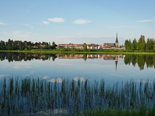 Mora Församling Church in Sweden reflecting in the Water on a bright morning. - obrazy, fototapety, plakaty