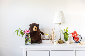 A teddy bear, a wooden hare, a bouquet of flowers, books on a white chest of drawers in the...