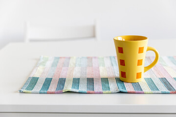 a yellow cup with a red geometric pattern on a napkin on a white table in the interior of the room.