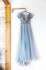 Fototapeta na wymiar A long grey bridesmaid dress with embroidery and sequins is on a hanger on the wall