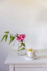 Plumberia rumba in a coffe cup, eucalyptus branch in a vase and cup of coffee on a white table against a wall with two frames. Ready layout. Vertical frame. Space for text