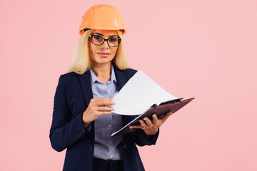 Portrait of attractive mature business woman architect or engineer in glasses use folder with documents on the pink background