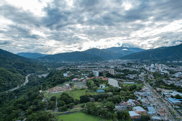 Colombia - Ibague, vista de dron con una montaña, la ciudad de ibague, una carretera en la mitad y un maravilloso cielo y nubes. - obrazy, fototapety, plakaty