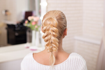 
Female back with blonde braid hairstyle on hairdressing salon background