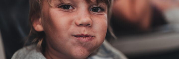 Obraz premium little candid kid boy five year old eats burger or sandwich food sitting in airplane seat on flight traveling from airport. children take a bite. child in air plane eating lunch or dinner meal. banner