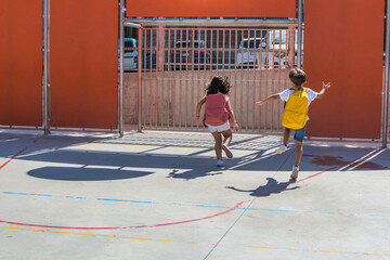 Elementary age children playing in the schoolyard. Girl and boy with school bags running and jumping. Back to school. Image with copy space.