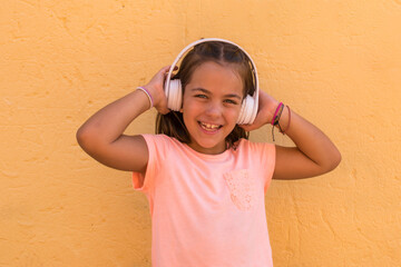Smiling little girl in school age listening to music with wireless headphones.  Preschool girl on...