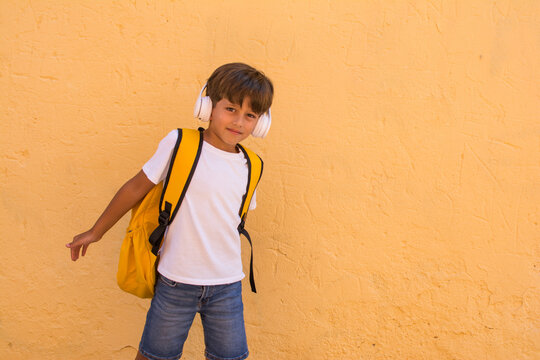 Little Boy 7 Years Old With Headphones And Backpack On A Yellow Background.