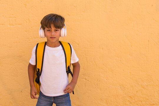Elementary age smiling boy listening to music with wireless headphones. Little boy on yellow background. Positive emotion. Image with copy space.