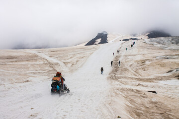 Tourists climb the snowy road to Elbrus among the fog and cloudy sky in the northern Caucasus in russia