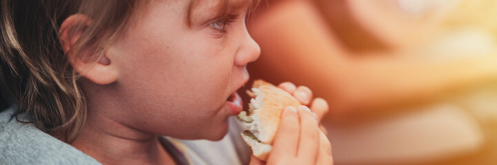 little candid kid boy five year old eats burger or sandwich food sitting in airplane seat on traveling from airport. children take a bite. child in air plane eating lunch or dinner meal. banner. flare