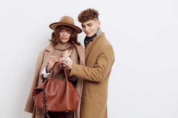 a sweet couple in love, a man and a woman in stylish autumn clothes stand on a white background and a guy helps hold a heavy woman's bag
