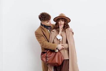 a beautiful, loving couple of a man and a woman stand on a white background in stylish autumn clothes, gently embracing and the woman joyfully holds her hand near her face