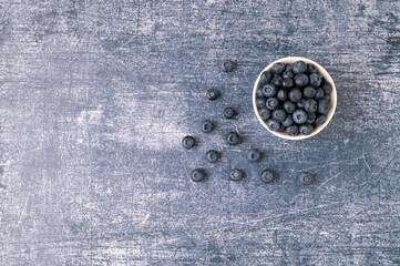 Blueberries in a white bowl surrounded by blueberry berries on a blue metallic background. Top view.