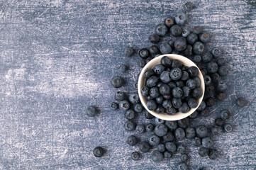 Close-up of a blueberries in a white bowl surrounded by blueberry berries on a dark blue metallic background. Top view.