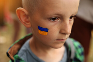 close up of smiling child with painted Ukrainian flag on face. Protest against Russian war invasion in Ukraine. Ukrainian Flag, Protesters concept