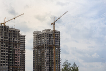 Fototapeta na wymiar Unfinished multi-storey residential buildings with scaffolding and construction cranes against a cloudy sky. Background with empty space for your text