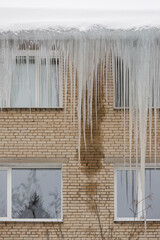 Large icicles hang from the roof of the house. Violation of the technology of thermal insulation of the roof and visor. Huge icicles are life-threatening