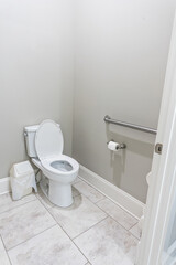 Fototapeta na wymiar A small half bathroom with gray walls and a toilet with tile floors in a new construction house with a handicap railing