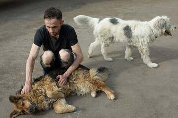 Guy with two dogs. Guy hugs stray dogs. Dogs on street. Man helps animals.