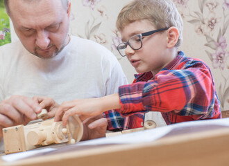 Happy father's day and childhood concept. Father and son-boy in glasses work with hand tools, using a screwdriver, assembling a wooden constructor at home at the table.