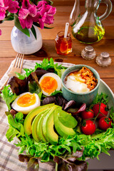 Salad with greens, avocado, eggs, tomatoes and tiny bowl with yogurt and granola, olive oil bottle