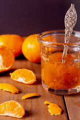 Tangerine jam on a tiny glass cup with fruit, wood surface.