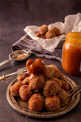 .Doughnuts on a silver plate with dulce de leche with cinnamon and sugar, on a grey background with silver fork and sifter