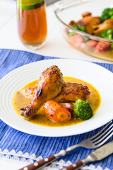 Chicken leg with vegetables on a white plate with silveware and blue linen on a white surface