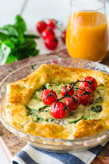 Rustic galette with tomatoes, zuchinni in a glass tray, rustic wood table, white surface, basil and tomatoes and juice