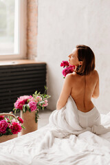 view from back. sexy topless woman with a bouquet of peonies in a blanket on bed