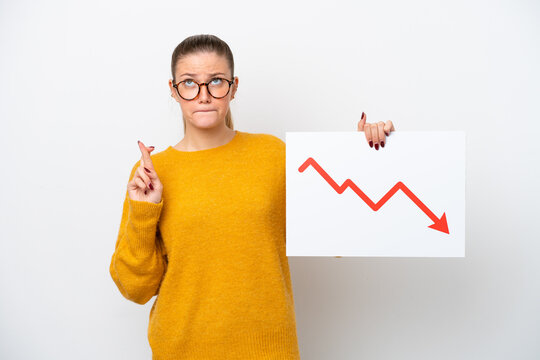Young caucasian woman isolated on white background holding a sign with a decreasing statistics arrow symbol with fingers crossing