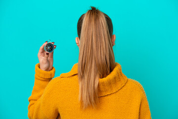 Young caucasian woman holding compass isolated on blue background in back position