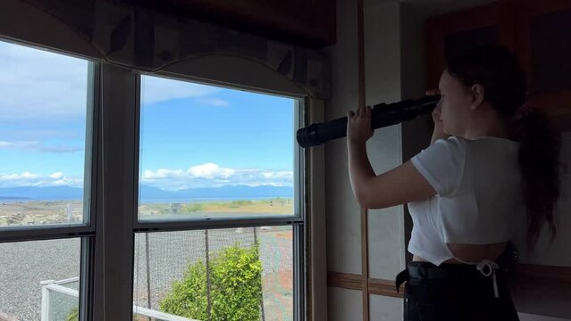 a teenager A girl stands in the trailer room and looks through a spyglass at the Pacific Ocean, looking for animals, the sea or ships, she is alone and bored but interesting Parksville beach