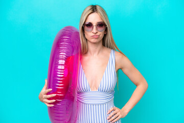 Blonde woman in swimsuit holding an air mattress donut isolated on blue background with sad expression