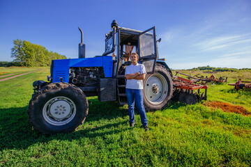 Farmer stands near the tractor on agricultural field