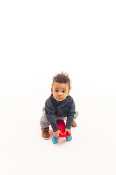 A little five years old afro-american guy sitting on a skateboard and looking into the camera - white background. High quality photo