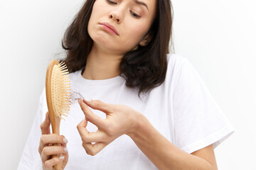 a close horizontal photo of a woman in a white T-shirt on a white background cleaning a comb from fallen hair, looking at the nh with the corners of her lips down