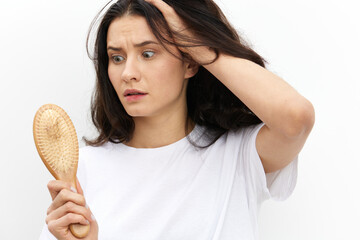 a sad, upset woman stands holding her head in panic and looks at a wooden massage comb