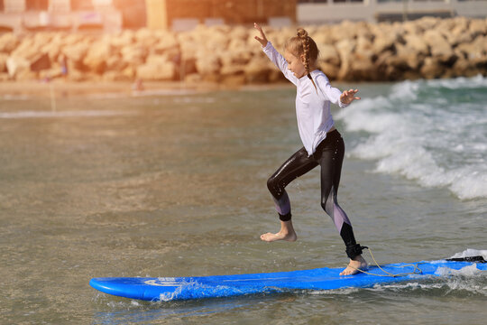 Happy baby girl - young surfer ride on surfboard with fun on sea waves. Active family lifestyle, kids outdoor water sport lessons and swimming activity in surf camp. Summer vacation with child