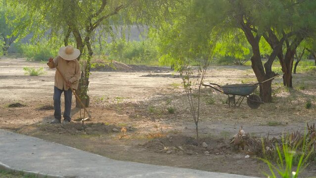 Hombre de sombrero trabajador preparando la tierra y limpiando en el campo