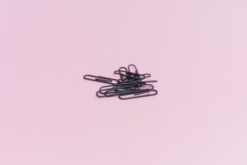 Clips negros para sujetar papel, sobre fondo rosa.