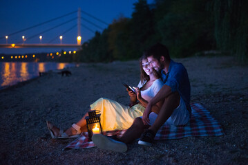 Young smiling couple having picnic on the beach at night