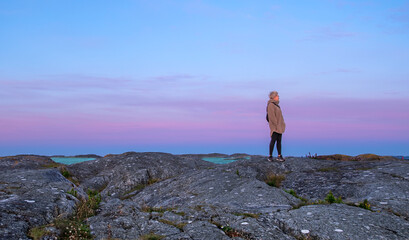 brightly colored pink-blue sky in front of the sunrise and a lonely figure of a man on a granite...