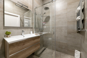 Bathroom with imitation marble tiles, shower cabin with sliding glass doors, frameless mirror on...