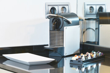 Corner of a black stone countertop in a kitchen with a pod coffee machine and mirrors on the wall