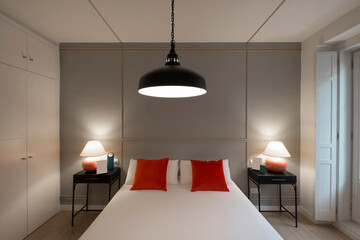 Bedroom with modern spartan-style furniture, built-in wardrobe and red cushions on the pillows on...