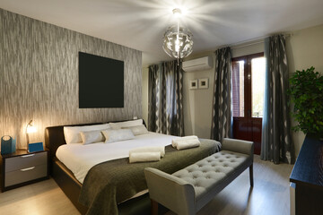 Bedroom with a double bed with a headboard upholstered in dark leather, with cushions on the cushions and a shoe-removing chair